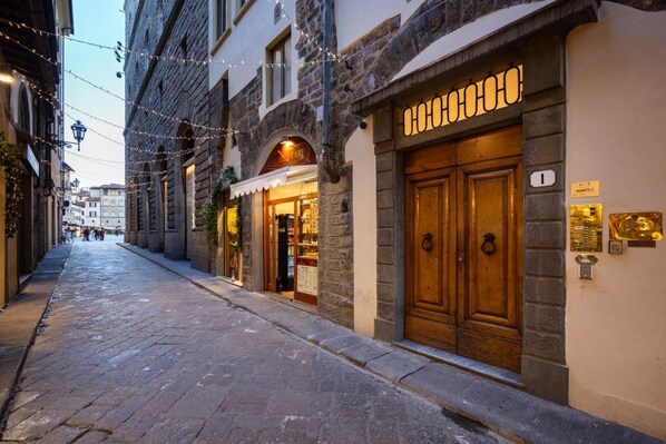 A cobblestone street with historic buildings, a shop with a wooden door, and string lights. - Calimaruzza Apartment - by Maison Florence (Firenze)