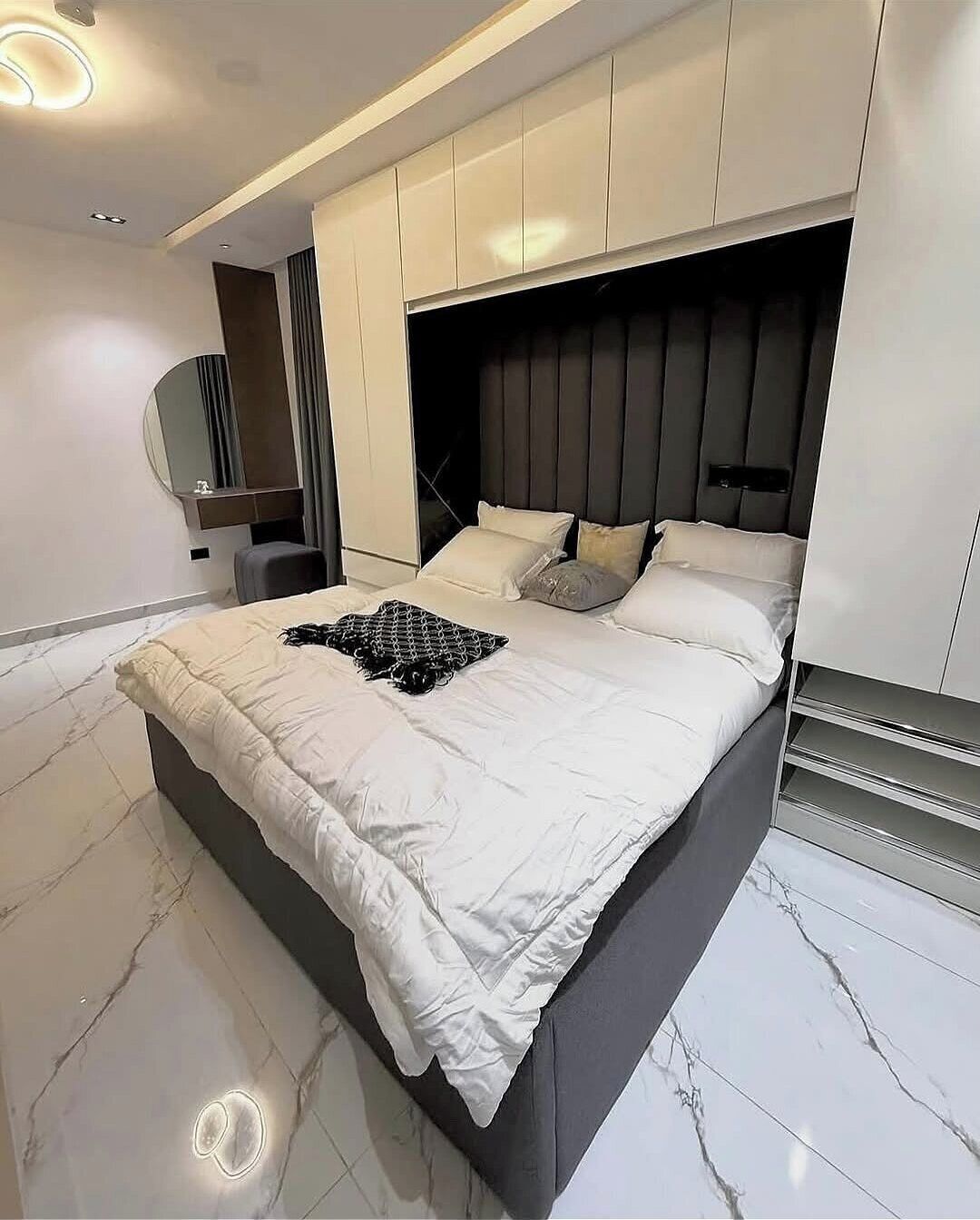 A modern bedroom with a large bed, built-in headboard, and a vanity with a mirror.
