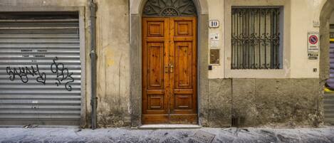 Una puerta doble de madera con arco superior, un cerrojo metálico a la izquierda y una ventana con barrotes a la derecha.