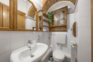 A bathroom with a white sink, a toilet, a mirror, and wooden cabinets. - Welcome to our enchanting medieval apartment located in the heart of Florence’s historic center, just 200 meters from Piazza della Signoria.This elegant apartment, perfect for families and couples, will offer you a unique and comfortable experience.The (Firenze)