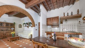 Un intérieur rustique comprenant un coin repas, une cuisine et un espace de vie, avec des poutres apparentes, un sol carrelé et une décoration traditionnelle.