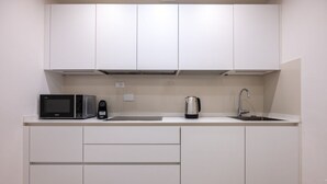 Cozinha moderna com armários brancos, micro-ondas, cafeteira e pia.