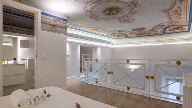 Quarto de hotel com uma cama grande, banheiro com espelho e teto com desenhos decorativos.