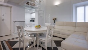 Uma sala moderna com um sofá branco, uma mesa de jantar com cadeiras, e uma escada em espiral que dá acesso a um andar superior.