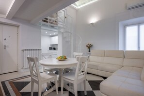 A modern living room with a white sofa, a dining table with chairs, and a spiral staircase leading to an upper level. - The White House - Home of the Frescoes (Firenze)