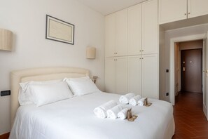 Ein Hotelzimmer mit einem großen Bett, weißen Laken, einem Kopfteil, einem Schrank und einem gerahmten Bild an der Wand.