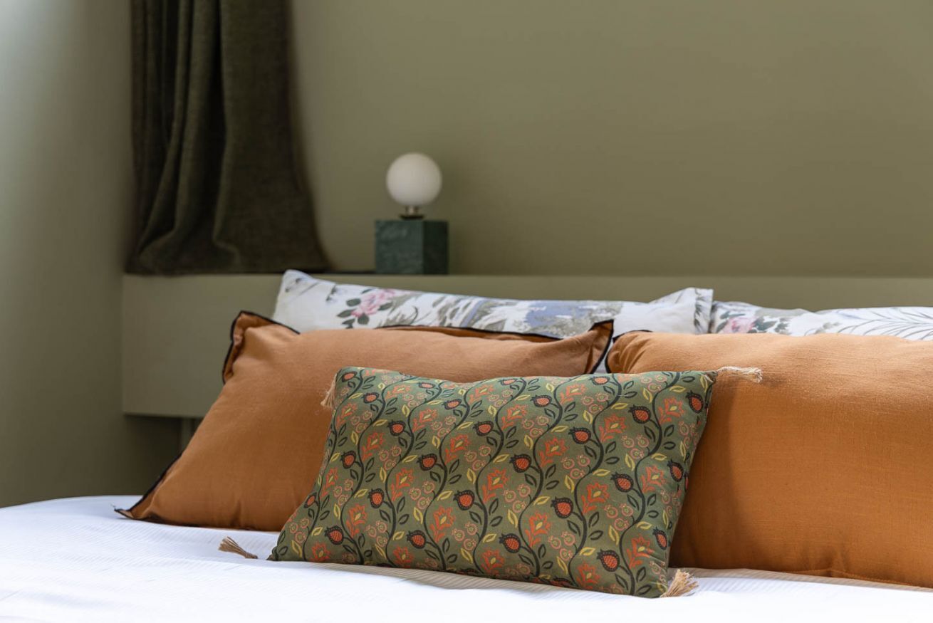 A bed with multiple pillows, a nightstand with a lamp, and a curtain.