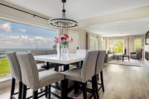 A modern dining area with a marble table, grey upholstered chairs, and a chandelier.