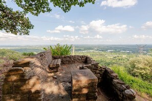 An ancient stone structure with a bench, surrounded by greenery and overlooking a distant landscape.