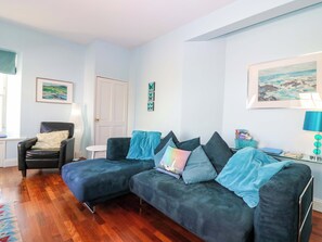 Ein Wohnzimmer mit einem dunkelblauen Sofa, einem schwarzen Ledersessel, einem kleinen weißen Tisch und einer Tür.