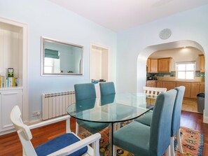 Un coin repas avec une table en verre et des chaises bleues, une cuisine avec des meubles en bois et un miroir au mur.