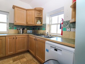 Une cuisine avec des meubles de rangement en bois, un grille-pain encastré, une bouilloire et un lave-vaisselle.