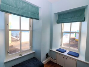 Ein Zimmer mit zwei Fenstern, jedes mit einem türkisfarbenen Vorhang, einer Bank und einem kleinen Regal mit einem blauen Kissen.