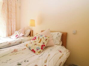 Ein Hotelzimmer mit zwei Betten, floralem Bettbezug, einer Nachttischlampe und einer Steckdose an der Wand.