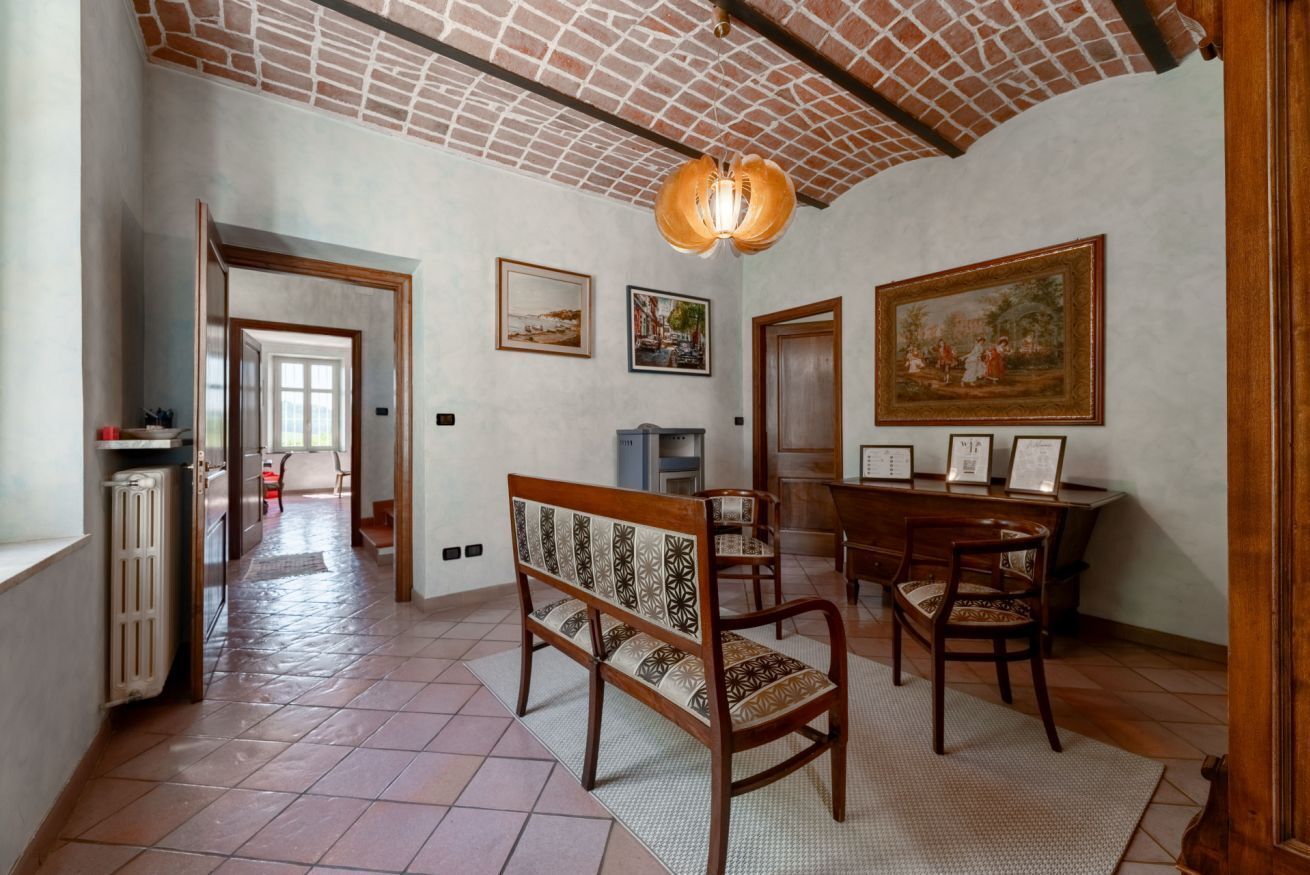 Una habitación amplia con suelo de baldosas, un banco de madera, una mesa de comedor con sillas y un cuadro grande en la pared.