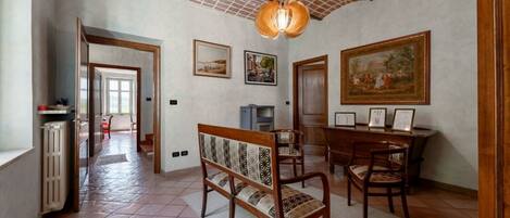 Una habitación amplia con suelo de baldosas, un banco de madera, una mesa de comedor con sillas y un cuadro grande en la pared.