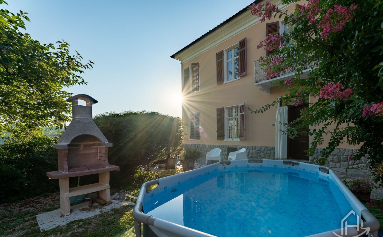 En swimmingpool, en grill og et toetagers hus med skodder.