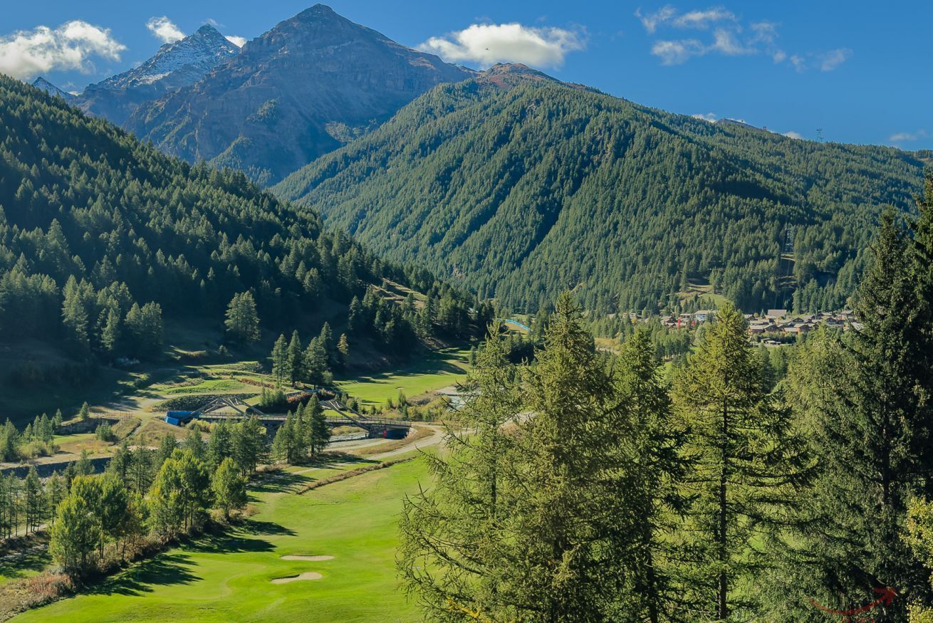 A mountainous landscape with a golf course, a small settlement, and a bridge.