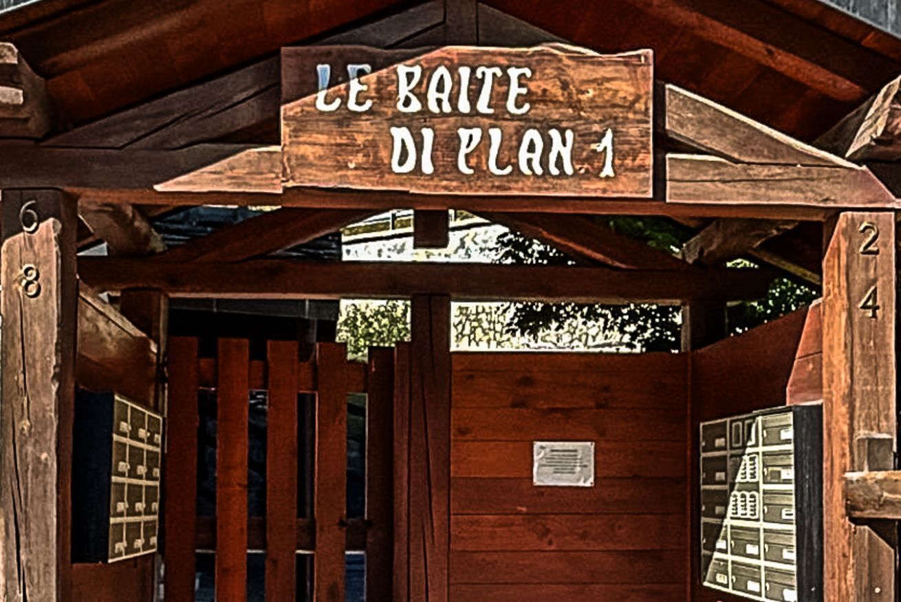 Uma placa de madeira com a inscrição 'LE BAITE DI PLAN 1', indicando uma sala ou área específica.