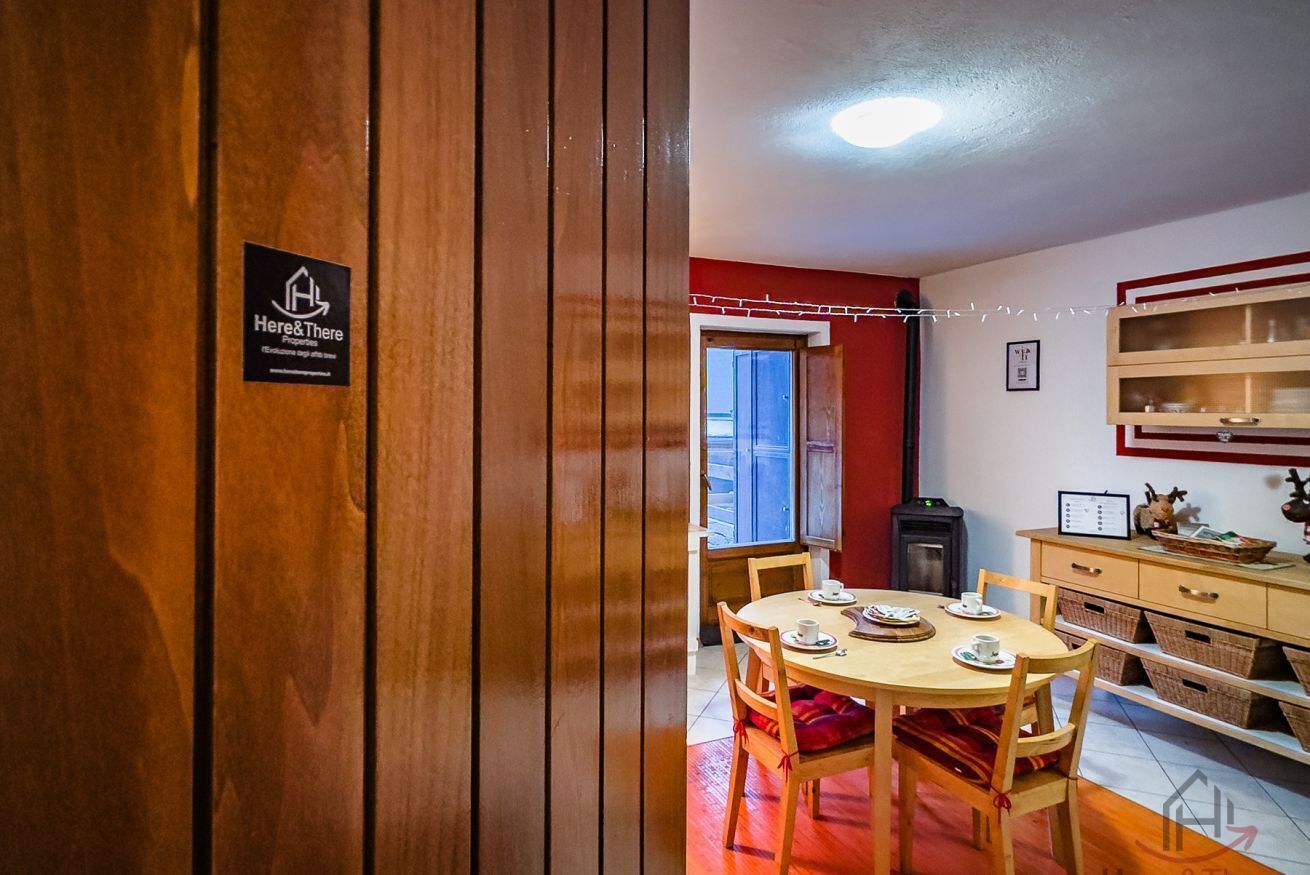 A wooden-framed room with a dining table set for two, a small kitchen area, and a window with a view.