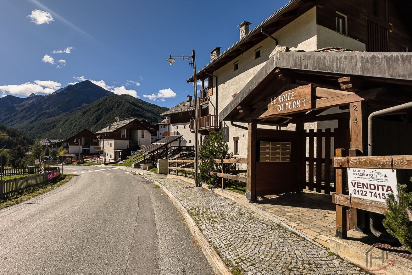 Une rue de village de montagne bordée de bâtiments en bois, avec une enseigne indiquant « LE BRITE DIENAN 1 » et une autre indiquant « VENDITA ».
