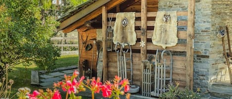 A rustic cabin with stone walls, wooden beams, and a porch with hanging items.