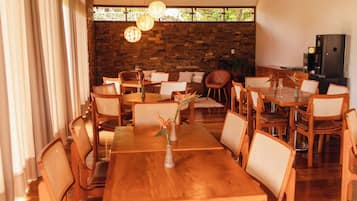Un comedor con mesas y sillas de madera, un muro de piedra y lámparas colgantes.
