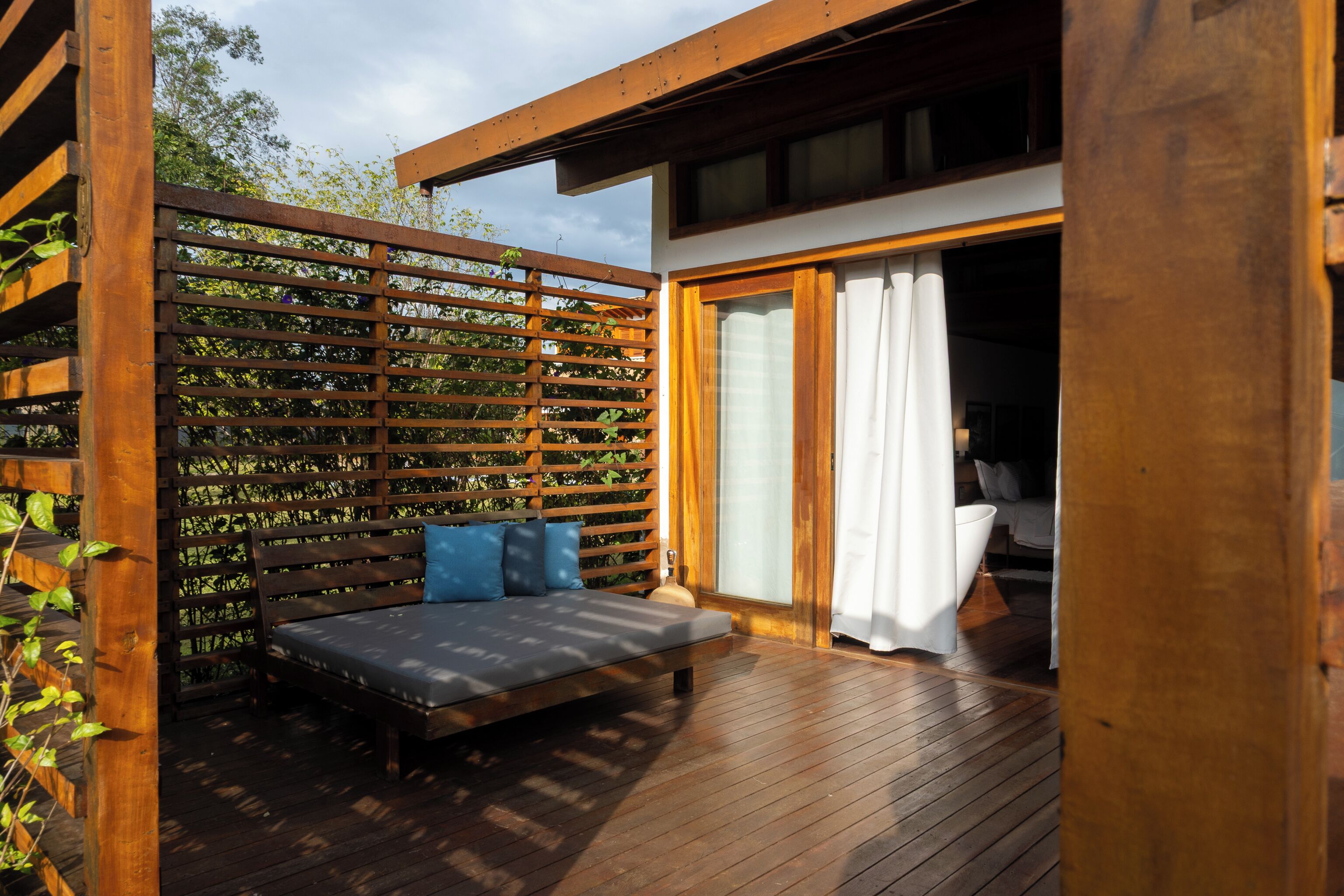 Um deck de madeira com um banco e uma porta de vidro que dá para um quarto.