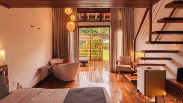 A modern hotel room with a wooden floor, a bed, a sitting area with a chair and a table, a small desk, and a staircase.