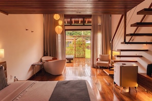 Ein modernes Hotelzimmer mit Holzboden, einem Bett, einer Sitzecke mit Stuhl und Tisch, einem kleinen Schreibtisch und einer Treppe.