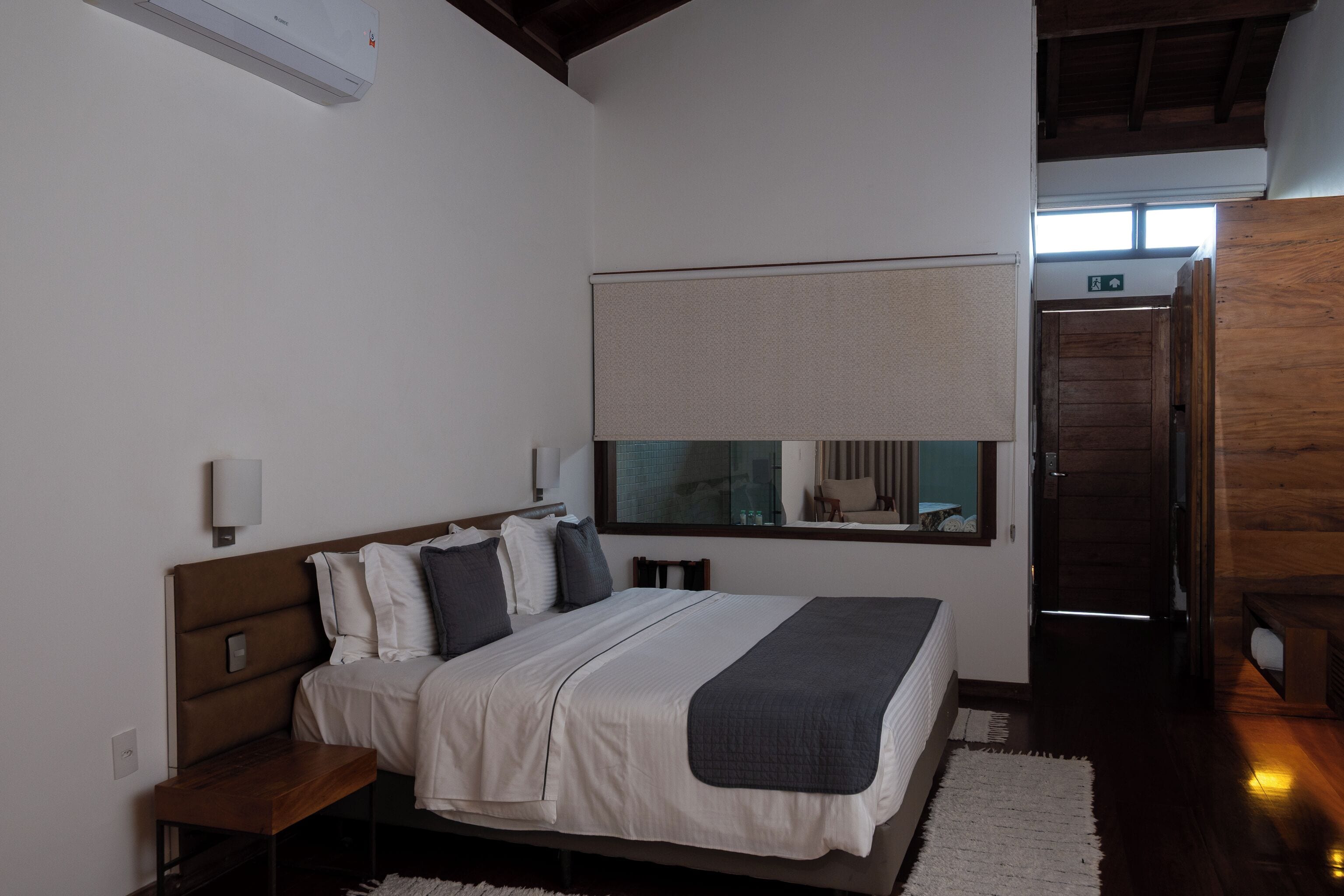 Un dormitorio con cama, mesitas de noche, una ventana con vistas y una puerta de madera.