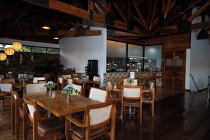 Interior de restaurante con mesas y sillas de madera, pared de piedra y lámparas colgantes.