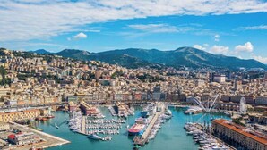 A coastal cityscape with a marina, buildings, and mountains in the background. - [Comfort Suite] Airport 5 min • A/C • Smart TV (Genova)