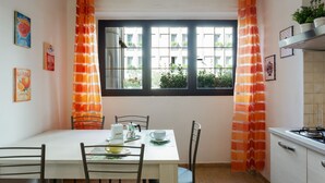 A dining area with a table set for four, chairs, a window with curtains, and kitchen cabinets. - GuestHost - Central Flat - Arno, Station and Duomo (Firenze)