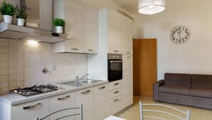 A modern kitchen with a gas stove, sink, and oven, a dining table with chairs, a sofa, and a wall clock. - GuestHost - Central Flat - Arno, Station and Duomo (Firenze)