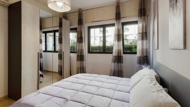A bedroom with a bed, a mirror, a window with curtains, and a hanging light fixture. - GuestHost - Central Flat - Arno, Station and Duomo (Firenze)