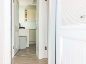 A hallway leading to a kitchen with white cabinets and a trash bin. - Lightkeepers Bothy (Eyemouth)