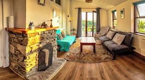 A cozy living room with a stone fireplace, a sofa, a coffee table, and a view through a large window.