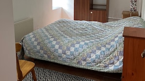 A bedroom with a bed, a wooden wardrobe, a window, and a patterned rug.