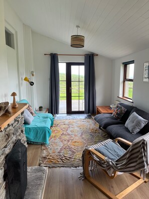 A cozy living room with a fireplace, a sofa, a rocking chair, and a large window with curtains. - Near to Durrus Cozy Apartment With a View (Dunbeacon)