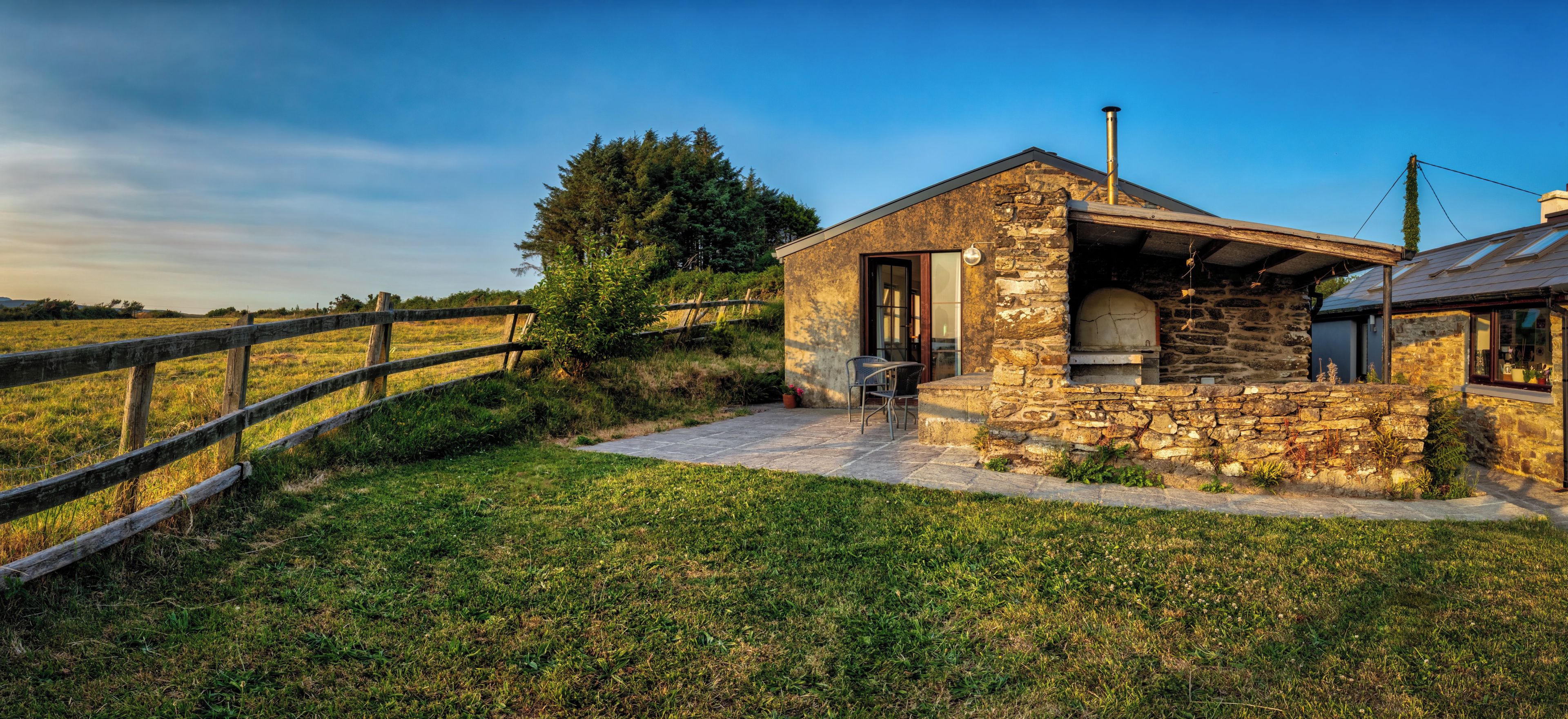 A stone building with a chimney, a wooden fence, and a grassy field.