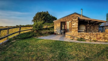 A stone building with a chimney, a wooden fence, and a grassy field.