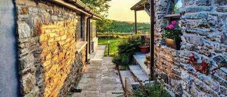 A stone pathway leading to a building with a wooden porch and flower pots.