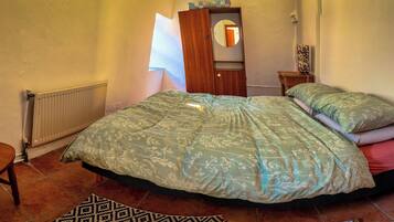 A bedroom with a bed, a chair, a dresser, a radiator, and a mirror.