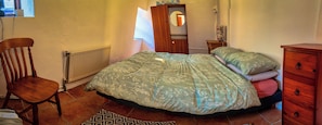 Un dormitorio con cama, una silla, cómoda, radiador y espejo.