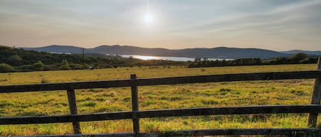 A grassy field with a wooden fence in the foreground and a body of water with mountains in the background.