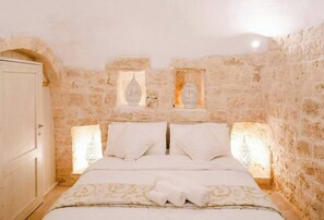 Ein Schlafzimmer mit einer Steinwand, einem Bett mit weißer Bettwäsche und zwei Wandleuchten.