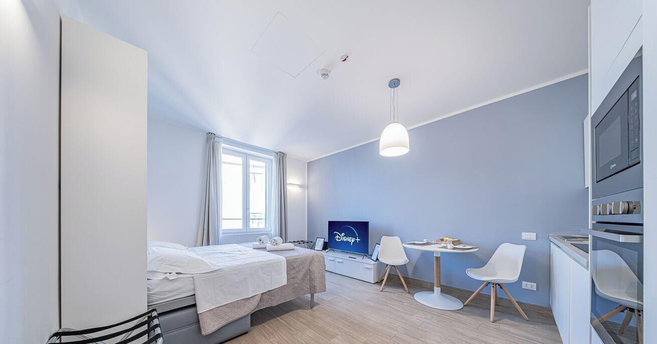 Une chambre moderne équipée d’un lit, d’une télévision, d’un bureau avec des chaises et d’une kitchenette.
