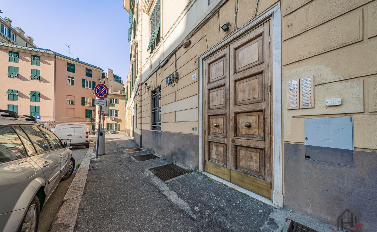 Une rue étroite bordée de voitures garées, une grande porte en bois et un immeuble doté de nombreuses fenêtres et de balcons.