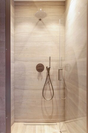 Eine moderne Dusche mit Glasabtrennung, einer Handbrause und einer wandmontierten Bedienarmatur.
